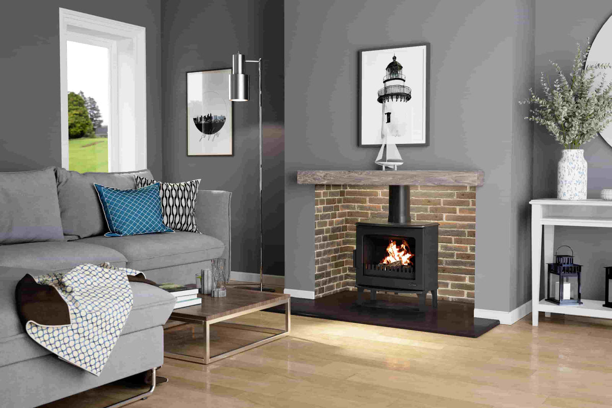 Black Carron ECO 5kW wood burning stove alight in a brick fireplace in a living room