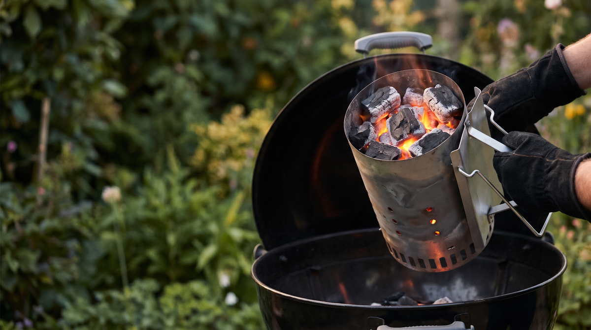 A metal chimney starter full of glowing lumpwood charcoal with edges just turning grey