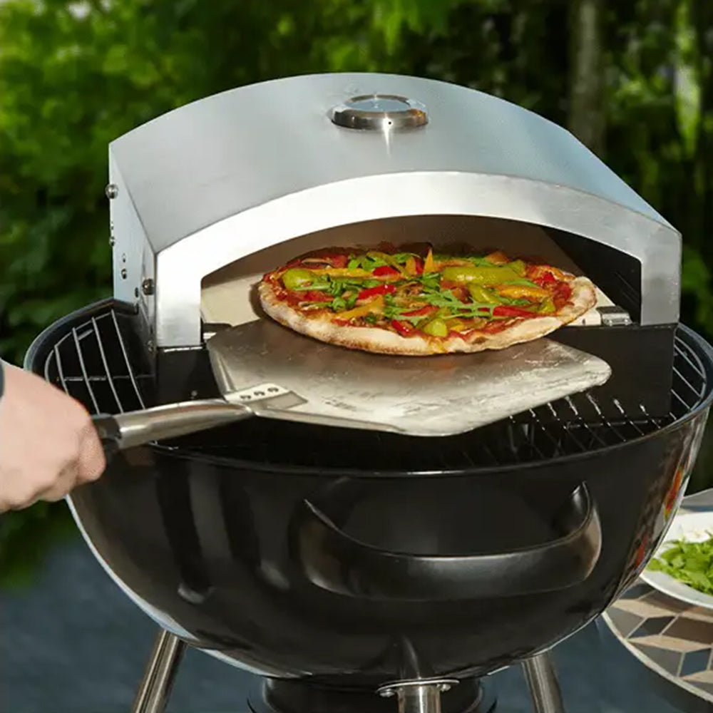 Artisan pizza oven insert on a kettle charcoal barbecue with a pizza on a peel