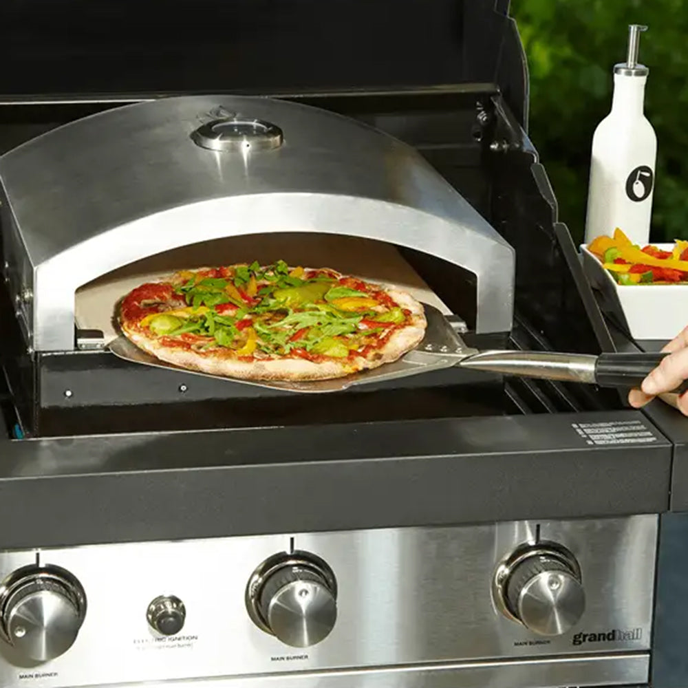 Artisan pizza oven insert on a gas barbecue with a pizza being loaded