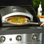 Artisan pizza oven insert on a gas barbecue with a pizza being loaded