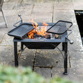 Firepits UK Box D square steel fire pit lit on a patio with both swing arm BBQ racks in place