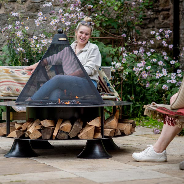 People sitting around a lit Flat Ring of Logs 120 fire pit on a patio