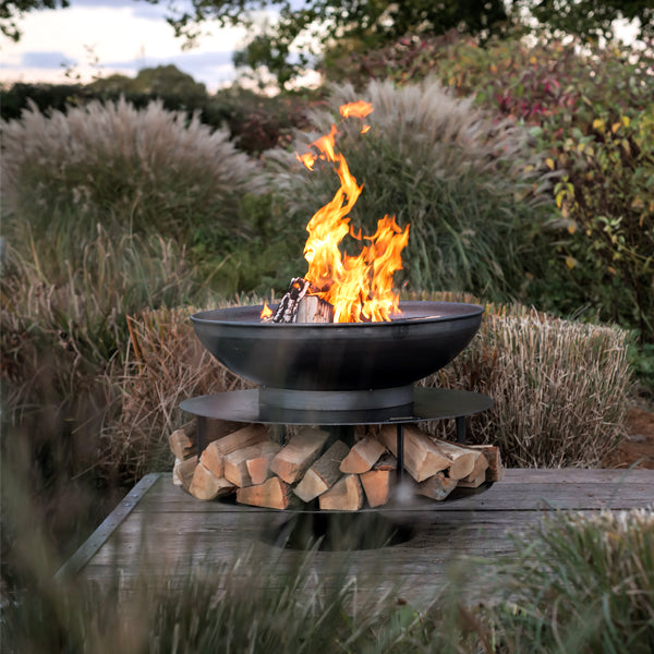Firepits UK Ring of Logs 90 fire pit lit on decking with logs stored in the base