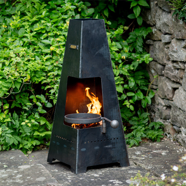 Piazza Junior chiminea lit on a patio with its swing arm BBQ rack