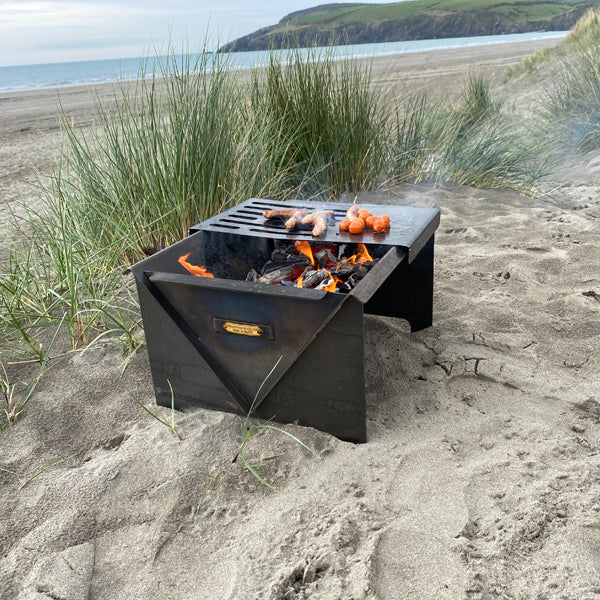 Cooking on the Flat Pack fire pit grill on a beach