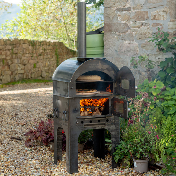 Firepits UK Modular Kitchen Tall Pizza Oven lit, with a pizza cooking and the fire cage open