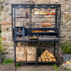 Firepits UK Asado Maximo fire table lit with food on the grill, rotisserie and hanging racks