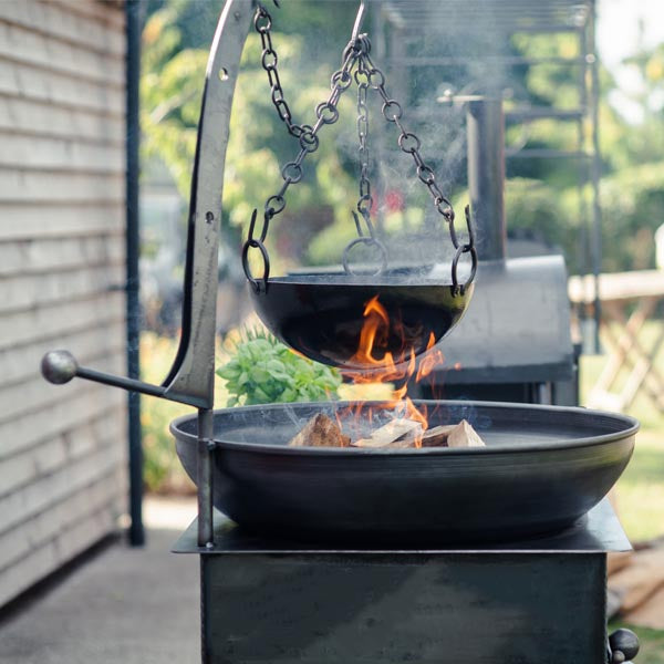 Hanging cooking bowl over the lit fire bowl of the Complete Outdoor Kitchen