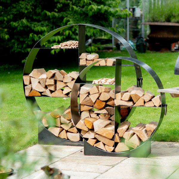 Two Firepits UK circular steel log stores filled with logs on a patio