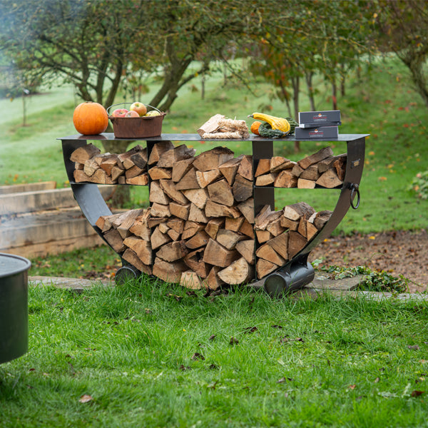 Half circular log store seen beyond a lit fire pit