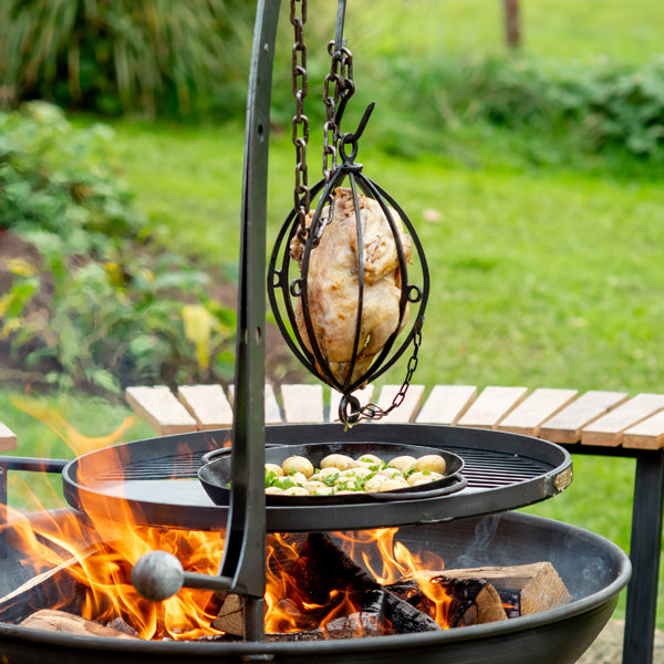Firepits UK hanging roaster holding a whole chicken, hung from a hanging arm over a fire pit