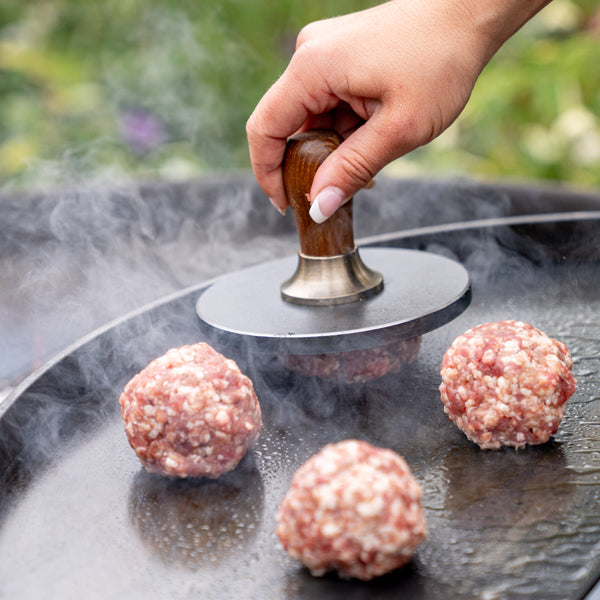 Burger press smashing a burger on a swing arm rack