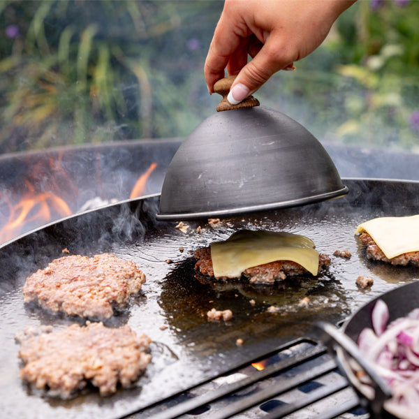 Burger cloche melting cheese over burgers on a fire pit rack