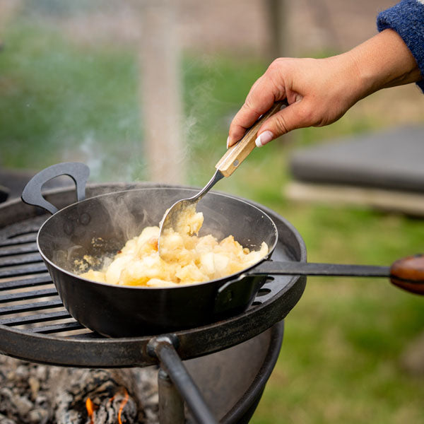 Long handled saucepan cooking peas over a fire