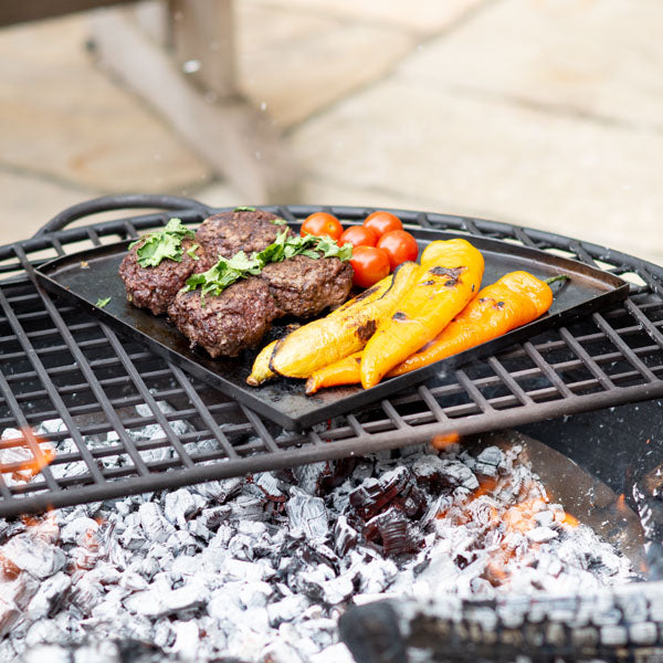 Burgers and peppers on a hot plate over a fire pit